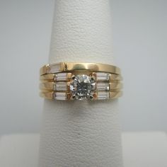 "For sale: (1) d895 Gorgeous 14k Yellow Gold Diamond Wedding Set PLEASE READ ENTIRE DESCRIPTION BEFORE PURCHASING Pre-owned item. Good condition. Please see pictures for details. Sold as is, as seen on pictures. This ring set contains eight (8) diamonds. One diamond is on the wedding band, and seven (7) diamonds are on the engagement ring. All diamonds except for the centerpiece are baguette cut. The centerpiece is round cut. Both rings are stamped. Specifics: 14k Yellow gold Total Diamonds: 0.9 Classic Bridal Set With Diamond Cut For Wedding, Gold Bridal Sets With Center Stone For Anniversary, Classic 14k Stamped Wedding Ring, 14k Stamped Diamond Wedding Ring, Classic Gold Bridal Sets With Center Stone, Stamped 14k Diamond Wedding Jewelry, Classic Yellow Gold Bridal Sets With Diamond Accents, Yellow Gold Bridal Set With Brilliant Cut For Marriage, Yellow Gold Bridal Set With Brilliant Cut