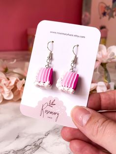 a pair of pink and white striped earrings on a card with flowers in the background