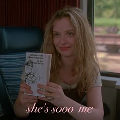 a woman sitting on a train reading a book with the words she's soo me