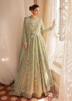 a woman standing in front of a window wearing a long green dress with gold embellishments