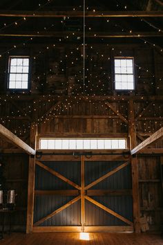 the inside of a barn with lights hanging from the ceiling and wooden doors that are open