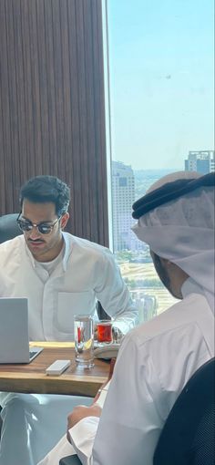 two men sitting at a table with laptops in front of them