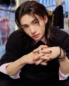 a young man with long hair wearing a black sweater and bracelets sitting on a couch