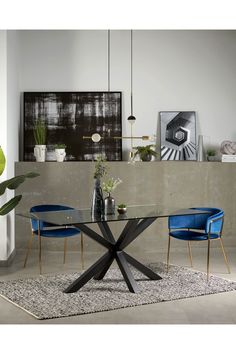 a glass table with blue chairs in front of a concrete wall and artwork on the wall