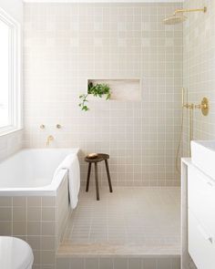 a white tiled bathroom with a stool next to the tub