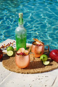 two copper mugs filled with apple cider next to a pool