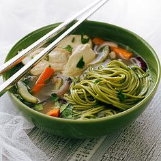 a green bowl filled with noodles and veggies next to two chopsticks