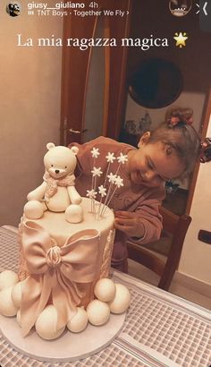 a woman is decorating a cake with white flowers and teddy bears on it while sitting at a table