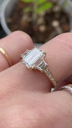 a close up of a person's hand with a ring on it and a plant in the background