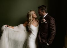 a man and woman standing next to each other in front of a green wall wearing wedding gowns