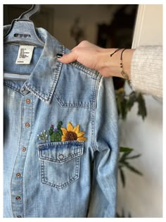 a person holding onto a jean jacket with a sunflower patch on it