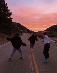 three people skateboarding down an empty road at sunset