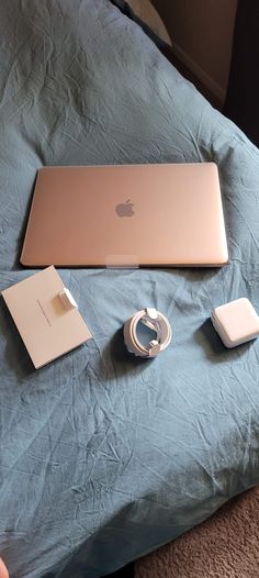 an apple laptop is sitting on a bed with other electronics and gadgets around it