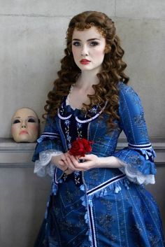 a woman in blue dress holding a red rose next to a doll's head