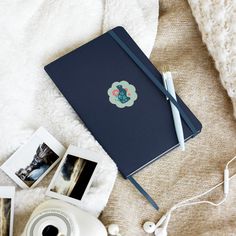 an open notebook sitting on top of a white blanket next to photos and a camera