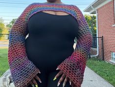 a woman in black top standing on sidewalk with her hands on her hips wearing a multicolored crocheted shawl