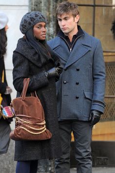 a man and woman standing next to each other on the street with one holding a purse