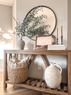 a wooden table topped with vases next to a mirror and a shelf filled with books