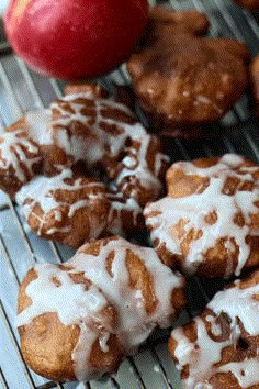 there are many donuts on the cooling rack with icing and an apple in the background