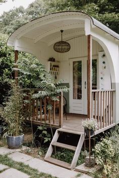 a small white house sitting in the middle of a lush green forest next to a door