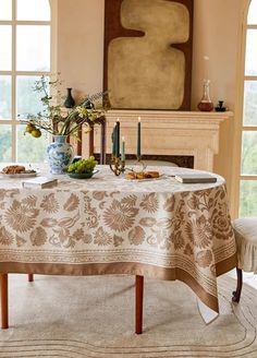 a dining room table covered with a white and brown tablecloth next to a fireplace