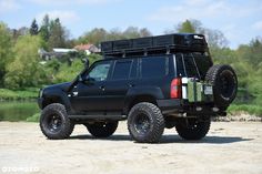 a black suv parked on top of a dirt road next to a lake and forest