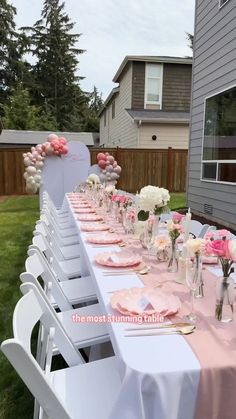 a long table with pink and white flowers in vases on the top is set up for an outdoor party