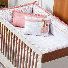 a white crib with pink and brown pillows on top of it's sides