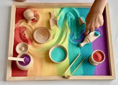 a child's hands are playing with sand and wooden spoons on a tray