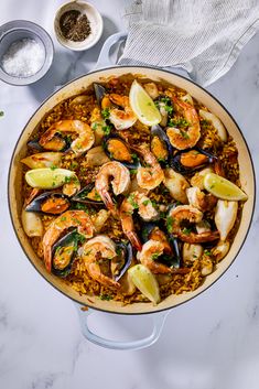 a pan filled with seafood and rice on top of a white counter next to two bowls