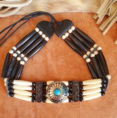 Concho Black Buffalo Horn and Antique Bone Hairpipe Bead Native American Indian style Choker with tie in back.  Includes black, bone and turquoise accent beads.  Order with or without 2" bone feather pendant or Concho Centerpiece.   Designed and handmade by me in the United States.  Approximately 14.5" (can be made shorter - just ask!)  Want it in a different color - just ask! See my other chokers:  https://www.etsy.com/shop/BlueEyesDesignsHB?ref=shop-header-name&listing_id=1184059251&section_id=31731787 You can also order a Genuine Horn and Bone hairpipe bead choker in the following colors (see my other listings): Black Horn Red Horn Amber Horn Turquoise Bone Bone (Natural) Bone (Antique) Black Horn with Dots Secondary color(s) can be almost any color combination of glass, wood, bone bead American Indian Jewelry Pearl, Comanche Indian Jewelry, Handmade Southwestern Style Choker, Native American Chokers, Native American Necklace Alltribes Indian Art, Native American Dentalium Necklace Shop, Bone Choker Native Americans, Bear Claw Necklace Native American, Vintage Native American Necklace