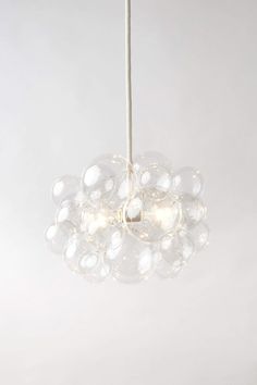 a light that is hanging from a string on a white wall and has bubble glass balls all over it