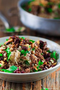 a close up of a bowl of food with rice and meat in it on a wooden table