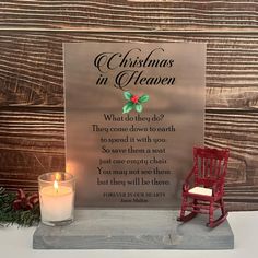 a christmas in heaven sign next to a lit candle on a table with pine cones