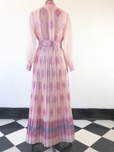 "1960's Alfred Shaheen pink oraganza maxi gown has an allover silver and pink foil print, with concentrated border motif at the hem and sleeve cuffs. There's a matching printed removable belt that has hooks and grommets for closure. The dress has a sunburst pleated skirt, unlined sheer bishop sleeves, and a button front and cuffs. The dress body is lined in a pink rayon that becomes an underslip in the skirt. Made in USA. 91% polyester, 9% nylon. Condition Excellent. Belt has wrinkling to vinyl Festive Pink Long Maxi Dress, Festive Vintage Pink Dress, Organza Maxi Dress, Alfred Shaheen, Pink Foil, Maxi Gown, White Stag, Body Dress, Maxi Gowns