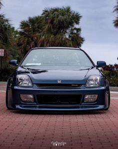 the front end of a blue car parked on a brick road next to palm trees