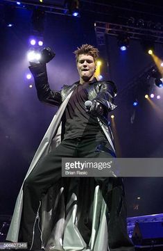 a man dressed in costume on stage with his hands up to the side and lights behind him