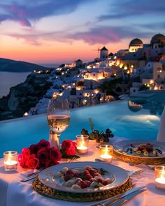 an outdoor dinner table with candles and plates on it, overlooking the ocean at dusk