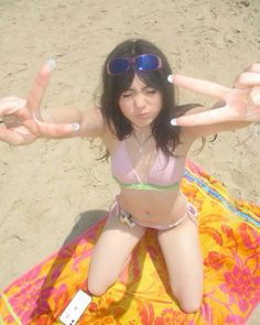 a woman sitting on top of a towel with her hands in the air and two fingers out