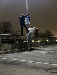 two people are hanging upside down on a street sign at an empty parking lot in the evening