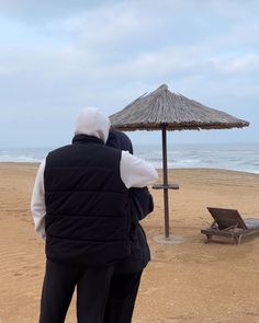 two people standing on the beach under an umbrella