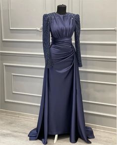 Elevate your evening elegance with our Exquisite Midnight Blue Gown, a perfect blend of timeless sophistication and modern glamour. Crafted from luxurious satin fabric, this gown features intricately embellished long sleeves adorned with delicate beadwork, adding a touch of shimmering magic to your look. The modest high neckline ensures a refined silhouette, while the pleated bodice accentuates your natural curves, offering a flattering fit that's ideal for formal occasions.The gown's unique des Long Sleeve Satin Gown With Sweep Train, Long Sleeve Satin Evening Gown, Long Sleeve Satin Evening Dress For Prom, Long Sleeve Satin Evening Dress For Prom Season, Satin Long Sleeve Evening Dress For Banquet, Long Sleeve Satin Evening Dress For Banquet, Embellished Long Sleeve Mother Of The Bride Evening Dress, Long Sleeve Embellished Satin Gown, Satin Long Sleeve Mother Of The Bride Evening Dress