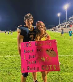 two people standing on a football field holding a pink sign that says i do not arguing about football it just think this is really cute