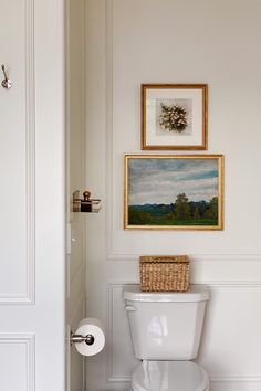 a white toilet sitting in a bathroom next to a painting