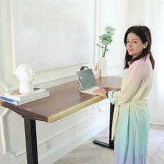 a woman standing in front of a desk with a laptop on it