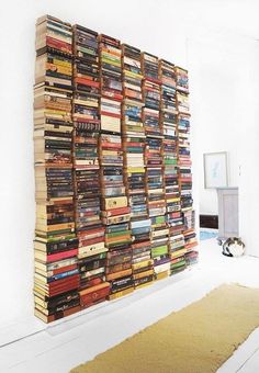 a large stack of books sitting on top of a white wall next to a rug