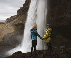 two women holding hands in front of a waterfall