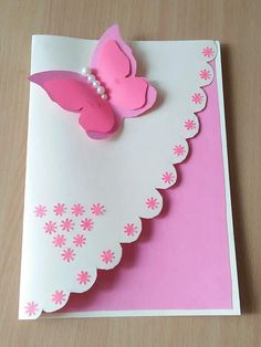 a pink and white greeting card with a butterfly on the front, sitting on a wooden table