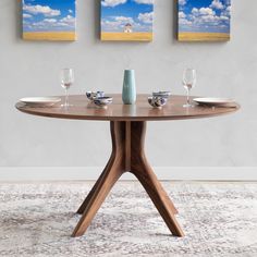 three paintings hang on the wall above a round table with wine glasses and place settings