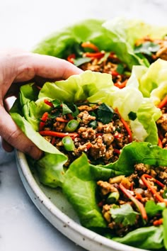 someone is holding lettuce leaves with meat and vegetables in it on a plate